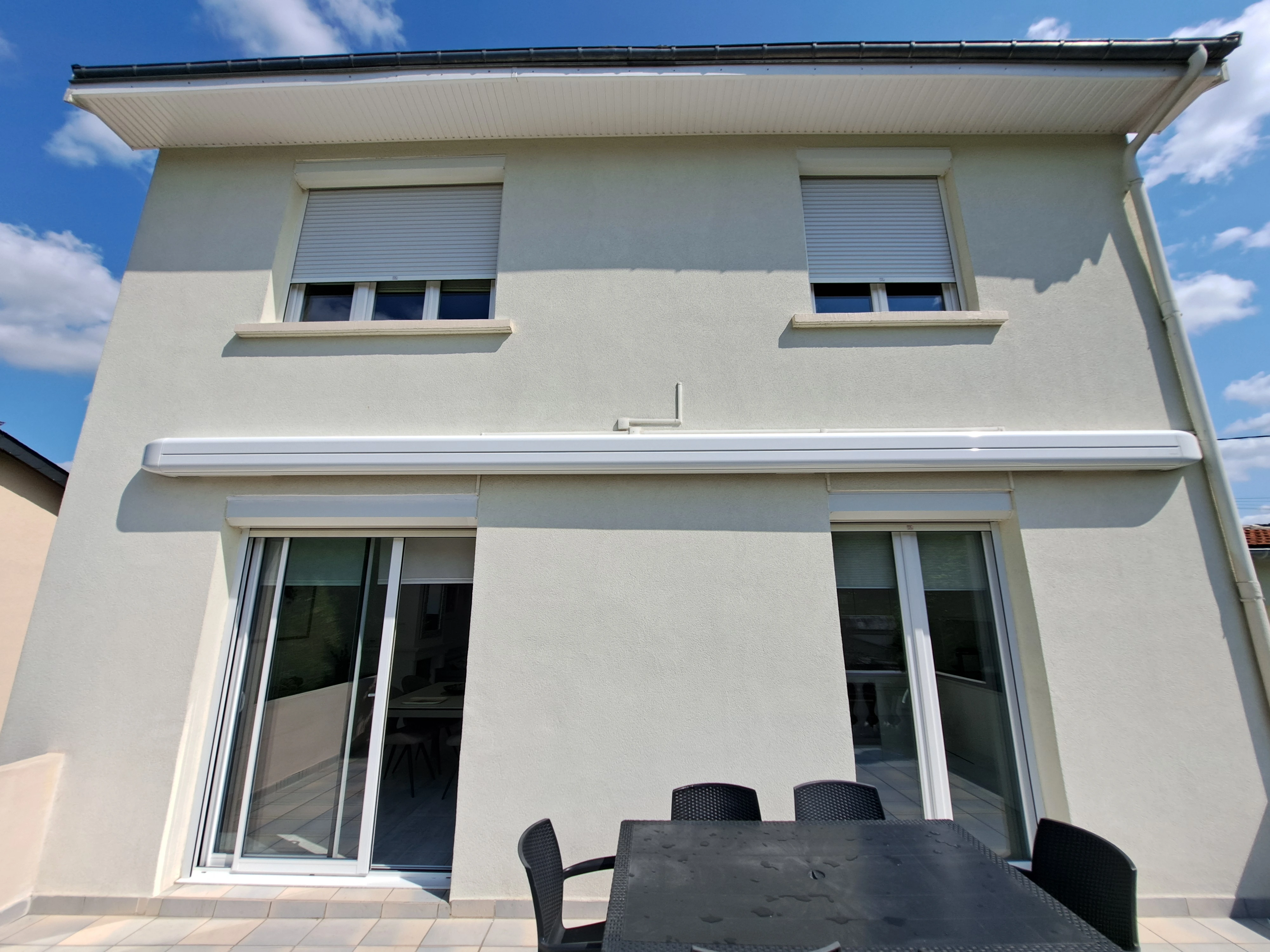 Façade avec Store Banne Vue frontale d'un store banne gris étendu sur un balcon avec balustrade blanche.